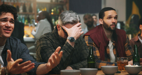 Obraz premium Disappointed, men and watching game in pub, unhappy and thinking of team failure, audience and upset. Frustrated, fans and people with alcohol in bar, sad and live stream of world cup or tournament