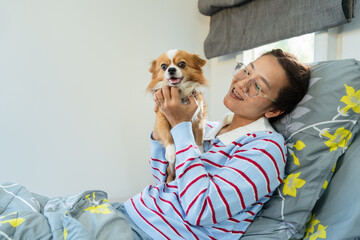 Happy Asian woman playing and holding cute Chihuahua dog on bed looking at each other with love and affection