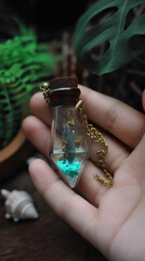 Unique Bottle Necklace with Resin Fish and Turquoise Sand Held in Hand, Close-Up of Miniature Art Jewelry with Cork Stopper and Gold Chain