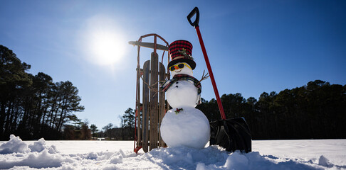 Winter scene with snowman with snow shovel and sled. Winter mood snowman in snowy field. Snowman helping to clean the snowy road. Winter vibes snowman decoration with shovel and sled.