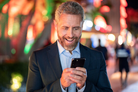 Businessman talk on phone at night city. Happy man in suit with phone in city. Businessman using phone. Businessman call on phone near city lights. Business call. Rich businessman in luxury setting. - Powered by Adobe