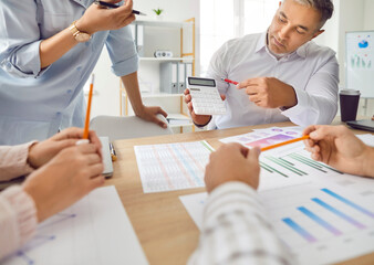 Close-up shot of male manager using calculator to show financial results report. Company employees sitting and discussing chart financial growth and business data, analyzing risks at office meeting.