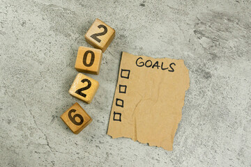 Paper with goal text and wooden cube blocks with 2026 text on gray background. New Year 2026 idea concept.