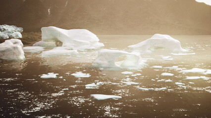 Early morning light casts a warm glow over a serene lake filled with floating icebergs. The majestic mountains rise in the background, reflecting natures beauty and tranquility.
