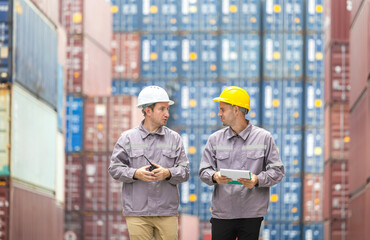 Logistics workers walking through container yard while discussing cargo tasks, Industrial staff and warehouse supervisors reviewing work plans in shipping container area