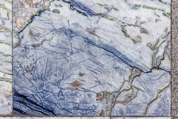 Close-up of aged and textured marble floor tiles featuring intricate patterns of blue and green veins on a white and light grey base, showing signs of wear and time.