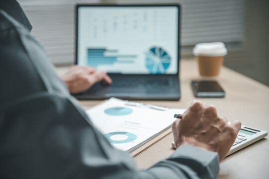 Close-up of a person working with financial documents, charts, and a calculator, representing corporate finance, budgeting strategy, revenue analysis, and professional accounting processes. - Powered by Adobe