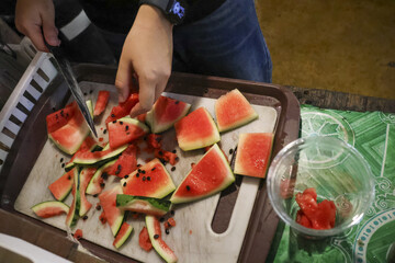 Close up of hand during food preparation, cutting fresh watermelon fruit into slices on tray. healthy and juicy snack creation for delicious, refreshing dessert