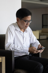Asian businessman waiting for his colleague who is coming late and start texting to ask the reason