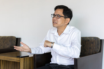 Asian businessman waiting for his colleague who is coming late, looking at the time and feeling upset, frustrated with the late comer