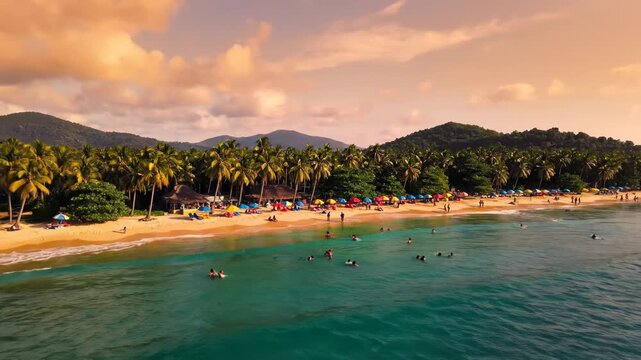 Aerial view of a crowded tropical beach at sunset with palm trees, colorful umbrellas, people swimming, and a jet ski on the sand