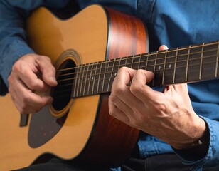Fototapeta premium Close-up of hands playing a wooden acoustic guitar, blue shirt