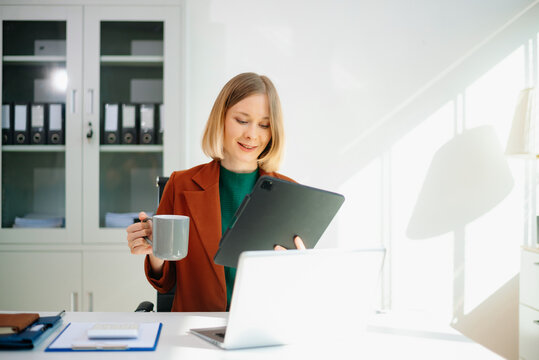 Professional woman on phone call in modern office, working on laptop.