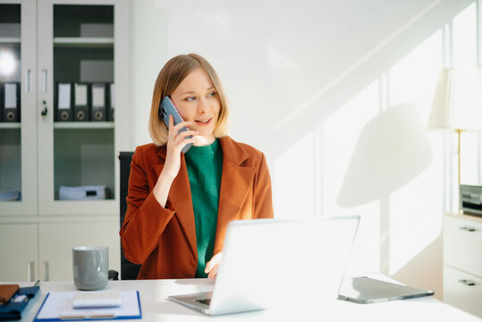 Professional woman on phone call in modern office, working on laptop. - Powered by Adobe