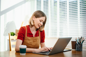 Caucasian woman working from her bright home office with laptop and documents.