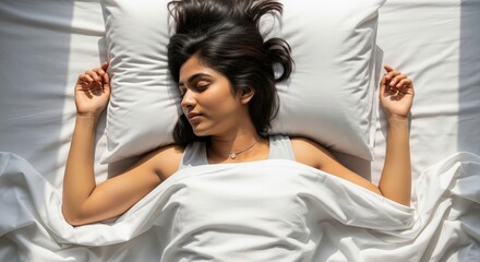 Overhead shot of young Indian female sleeping calmly in bright white sheets