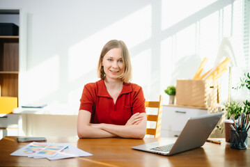 Caucasian woman sitting at her home office desk and looking at the camera. Great for remote work,...