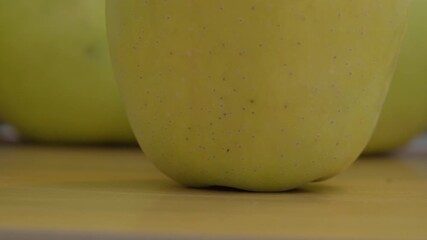 Detailed macro shot capturing the texture of a fresh golden yellow apple on a wooden table, accentuated by soft, natural lighting. Perfect for food, health, or organic lifestyle themes.