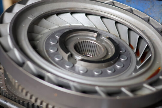 Detailed view of a metallic torque converter impeller or stator assembly, showing central splines, turbine blades, and an outer ring gear, representing complex hydraulic power transmission and repair.