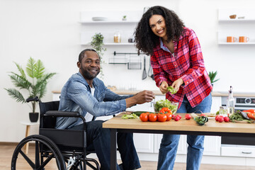 A smiling couple prepares a healthy meal in their bright, modern kitchen, with one person using a wheelchair.