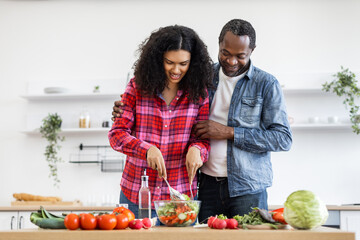 An African-American couple prepares a healthy salad together in a bright, modern kitchen, embracing a lifestyle of wellness and togetherness.