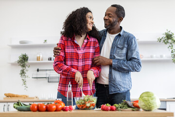 An affectionate couple prepares a healthy salad in a bright, modern kitchen setting, sharing a moment of connection.