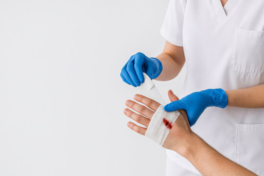 horizontal photo of a healthcare professional in blue gloves cleaning and bandaging a fresh wound on a patient&rsquo;s hand against a bright clinical background, offering a clear visual for medical care