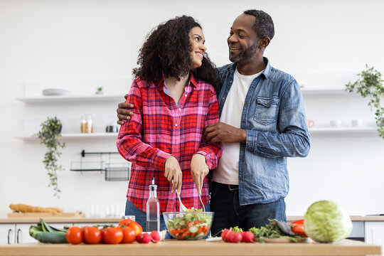 An affectionate couple prepares a healthy salad in a bright, modern kitchen setting, sharing a moment of connection. - Powered by Adobe