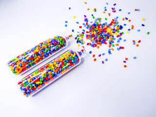 Colorful polymer masterbatch gradation, colorful pigment resin pellets in glass tubes poured on a white background, suitable as a product catalog design for industrial plastic manufacturing companies