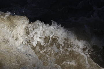 Powerful close up of turbulent churning water. rushing white foam and dark current create an abstract background showing raw power and motion of wild river