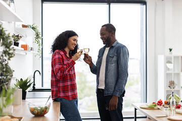 A smiling couple enjoys a toast with wine in a bright, modern kitchen setting. They are celebrating a special moment together.