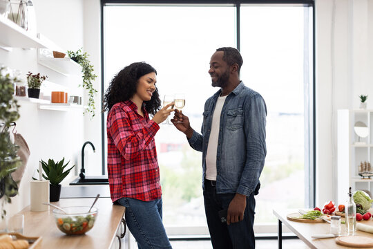 A smiling couple clinks glasses of wine in a bright, modern kitchen, celebrating a special moment together. - Powered by Adobe