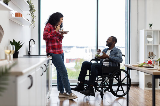 A diverse couple shares a meal in a bright, modern kitchen, with one person using a wheelchair.