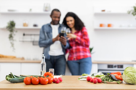 A couple enjoys a moment together in the kitchen, with fresh vegetables on the counter. - Powered by Adobe