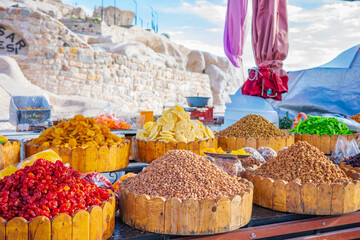 A vibrant and detailed photograph of assorted dried fruits and nuts arranged in wooden baskets at a traditional outdoor market in Turkey. The display includes dried apricots, pineapples, cherries