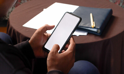 Close Up of Smartphone with white Screen Mock Up Display In Male Hands. Man Sitting In Home Browsing Internet , Watching Content, News, Financial Reports on Phone. 