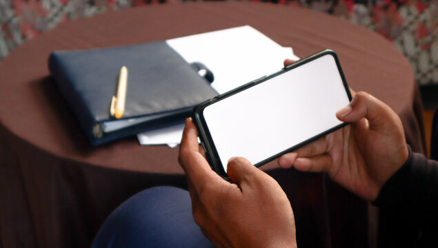 Close Up of Smartphone with white Screen Mock Up Display In Male Hands. Man Sitting In Home Browsing Internet , Watching Content, News, Financial Reports on Phone.