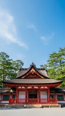 Obraz premium Traditional Japanese Shrine Architecture with Red Details and Lush Green Trees Under a Clear Blue Sky.