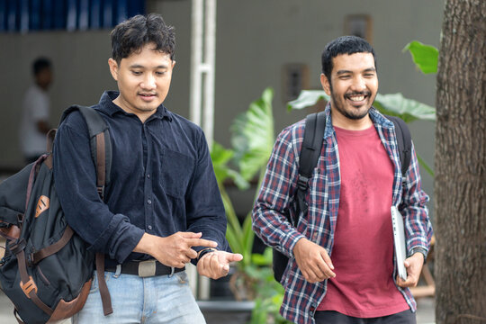 Two Asian men walking and discussing work outdoors - Powered by Adobe