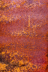 Metal surface with a thick layer of rust, exhibiting a predominantly purple hue with hints of orange and a rough texture