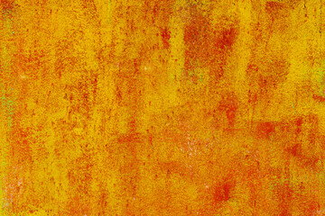 Close-up of a weathered rusty metal surface with a vibrant orange and yellow texture. The corroded iron shows peeling paint and oxidation, creating an abstract industrial background with a rough, aged