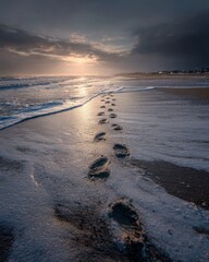 Footprints in wet sand leading toward the shoreline under a warm sunrise glow.