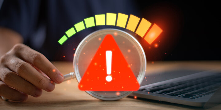 A digital warning alert symbol highlighted through a magnifying glass beside a laptop, representing cybersecurity risks, data threats, system notifications, and online protection awareness.