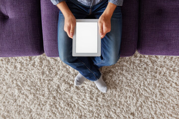 Top view A young man is sitting on the sofa in the living room with a tablet with an empty white screen