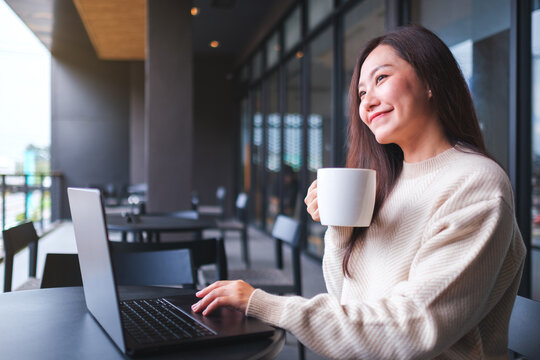 Portrait image of a woman working on laptop computer while drinking coffee in cafe