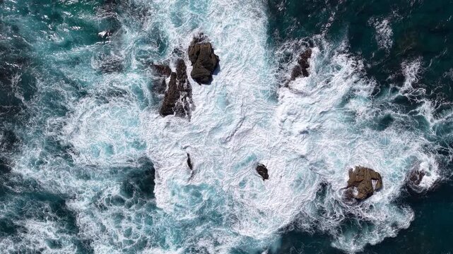 Aerial view of ocean waves crashing on rocky coastline, turquoise sea and white foam creating natural abstract pattern