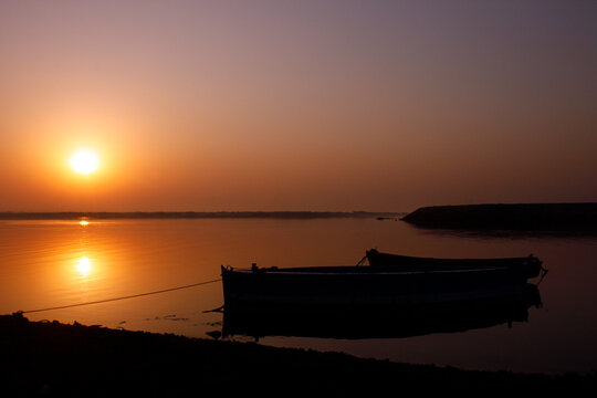 Boats anchored on calm water during a golden sunset on the Saurashtra coast of India. Peaceful, warm, and serene evening landscape.