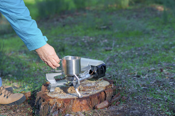 Person preparing hot drink using a portable stove and metal mug outdoors. Camping and cooking in nature