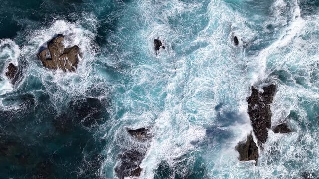 Aerial view of ocean waves crashing on rocky coastline, turquoise sea and white foam creating natural abstract pattern