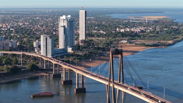High-altitude drone tracking right, focusing on the bridge towers against the river and the vegetated cityscape of Corrientes.